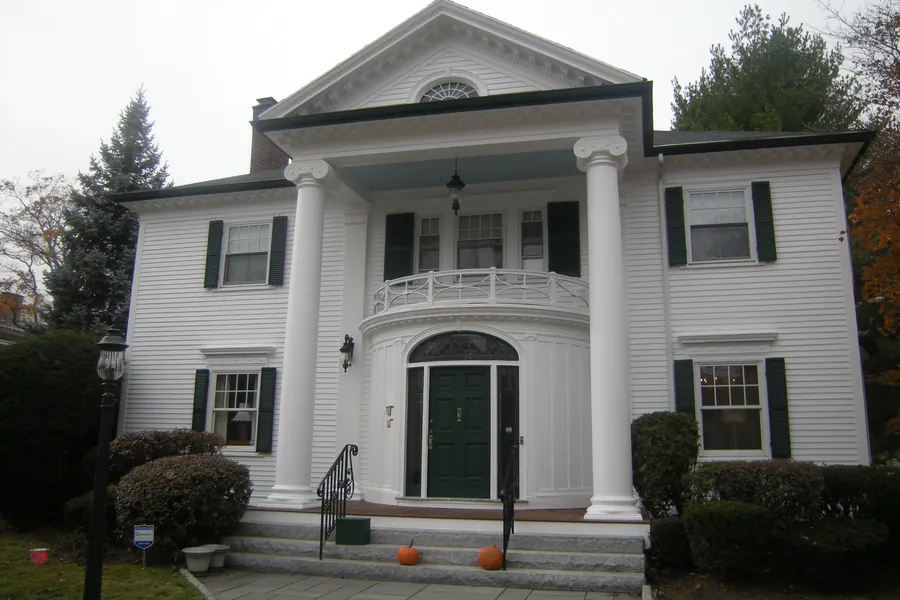 White clapboard-sided colonial house with black shutters and a columned entry